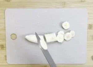 Slicing a banana on a cutting board with a knife, perfect for healthy snack preparation or recipe ingredients.